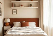 small bedroom with terracotta upholstered headboard, floating shelves, and storage ottoman