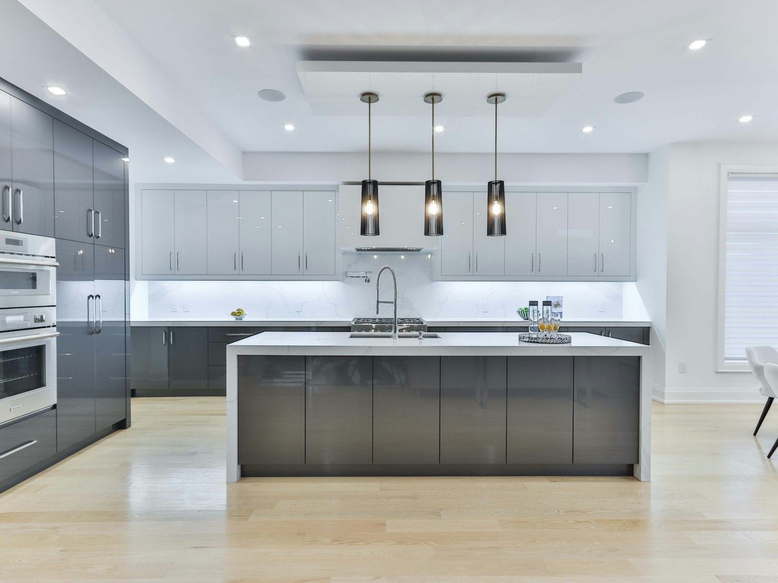 A modern kitchen with grey cabinets, a white island, and three pendants