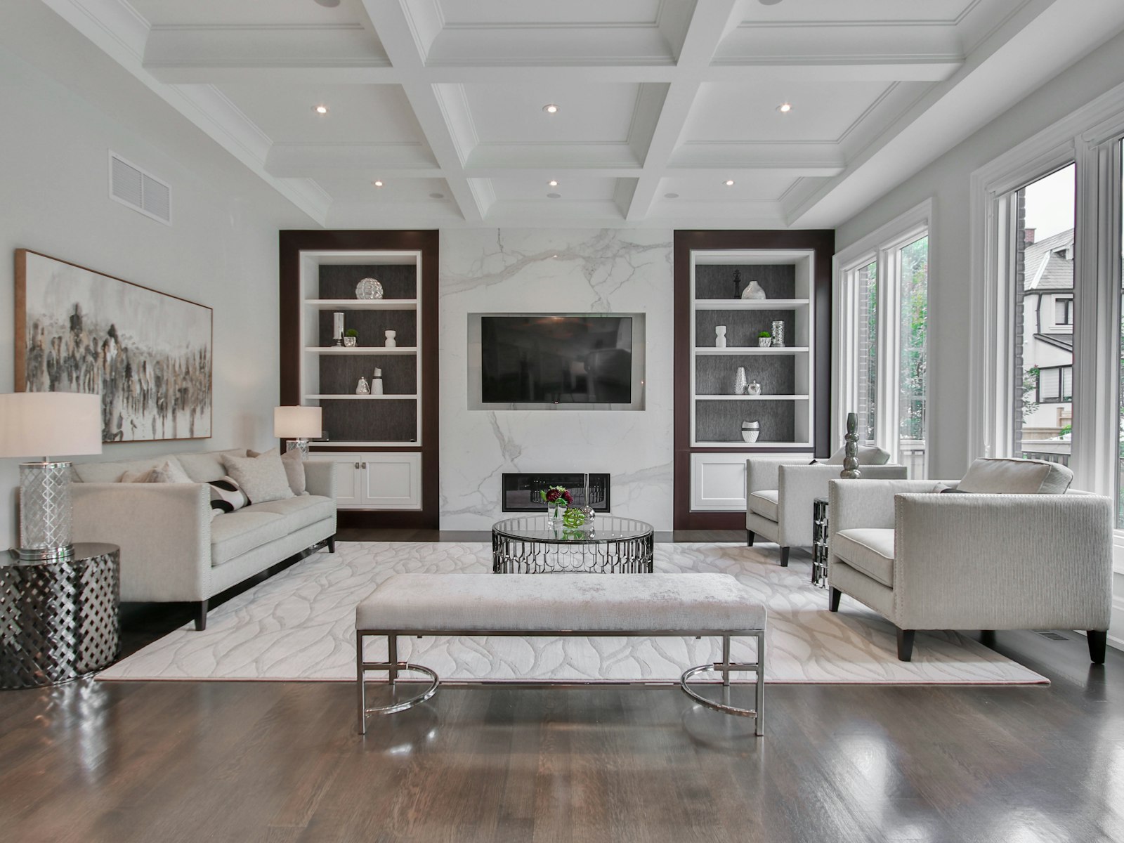 A living room with a marble fireplace, white sofas, and dark wood shelves