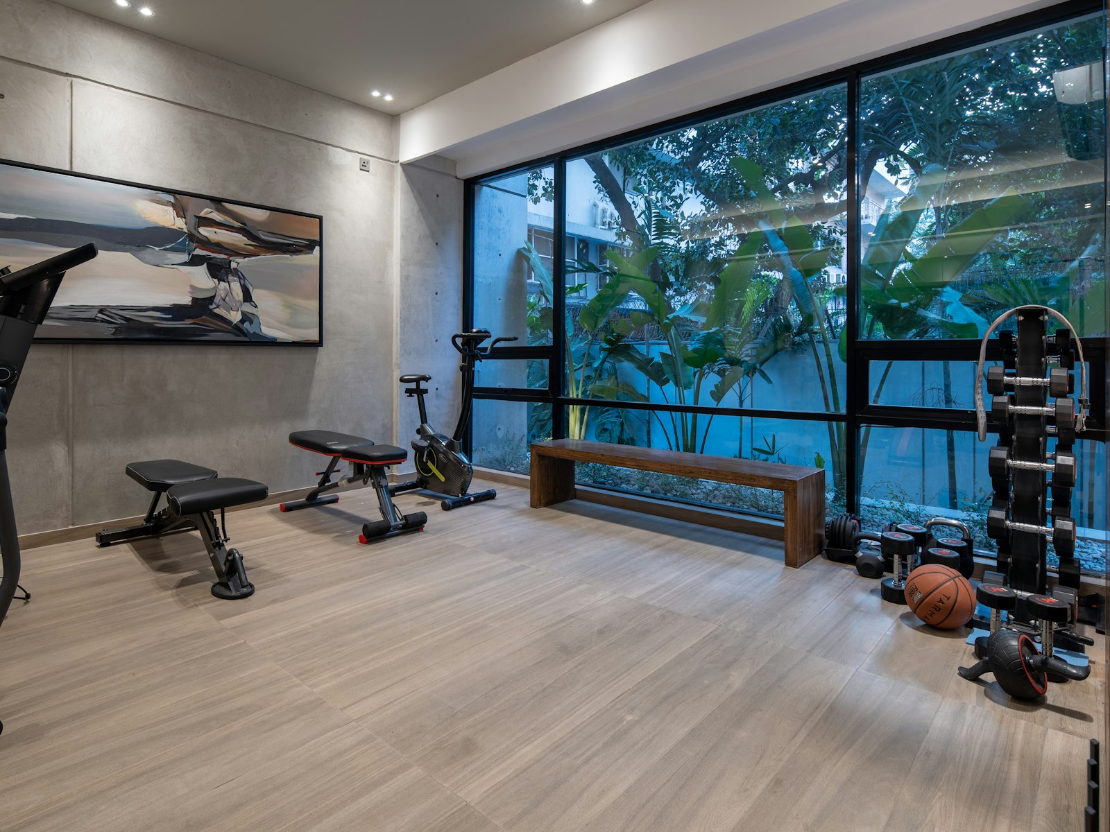 A home gym with exercise equipment, a wooden bench, and large windows