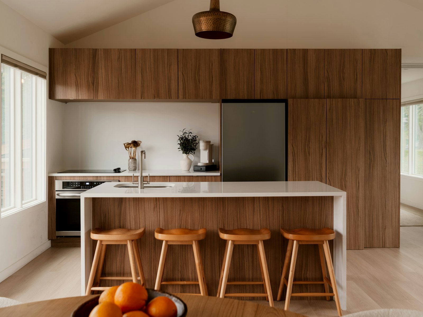 A modern kitchen with walnut cabinetry, a white island, and four wood stools