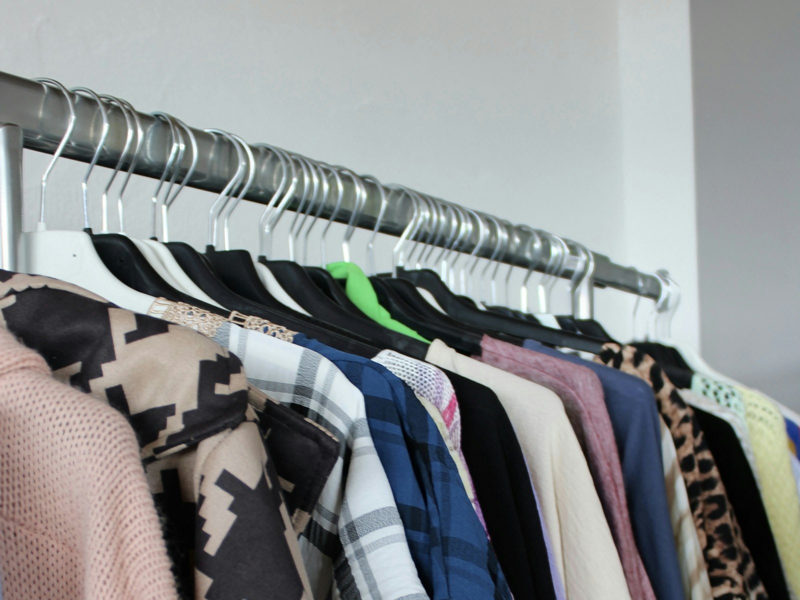 A row of garments hanging on a metal rack against a white wall