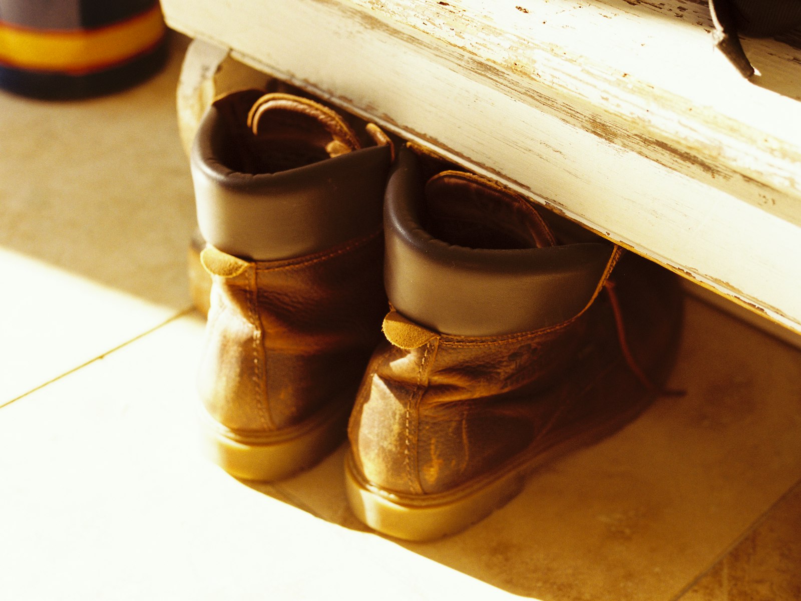 Worn leather boots under a bench in a sunlit hallway