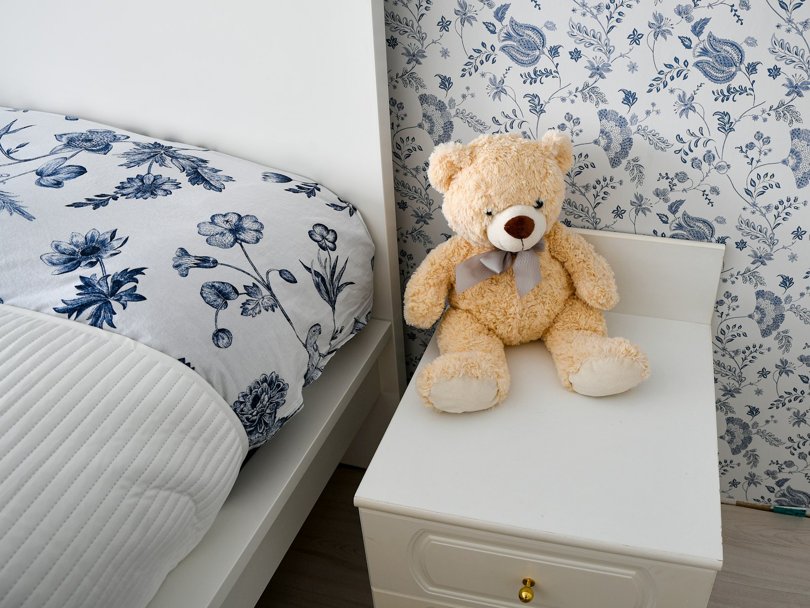 Teddy bear on bedside table with floral bedding and wallpaper