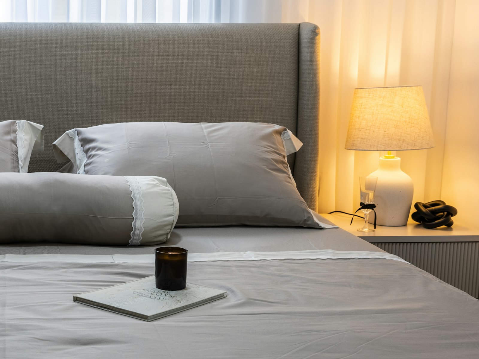 Warm bedside lamp and a candle beside grey bedding