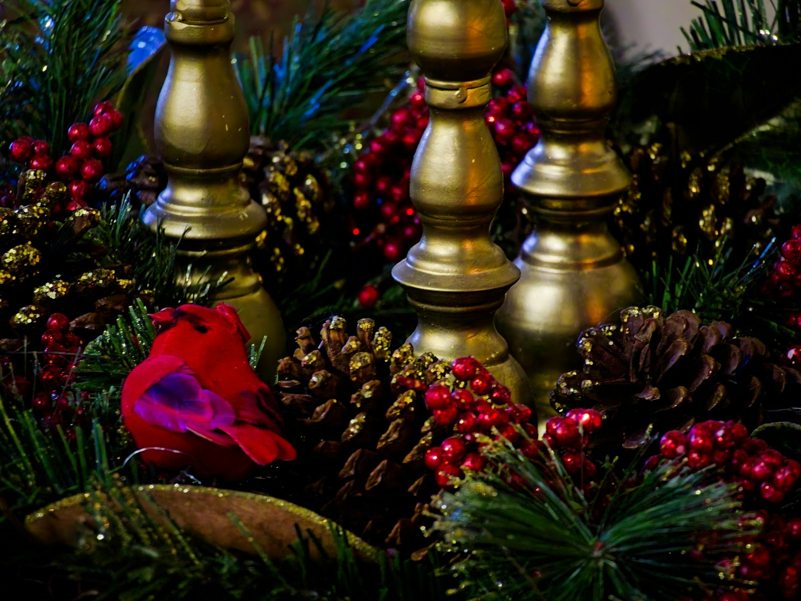 Brass candlesticks rising from a centerpiece of pinecones, berries and greenery