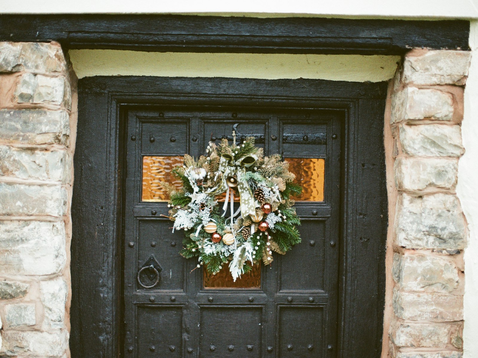 Dark front door with a natural Christmas wreath framed by a stone entryway