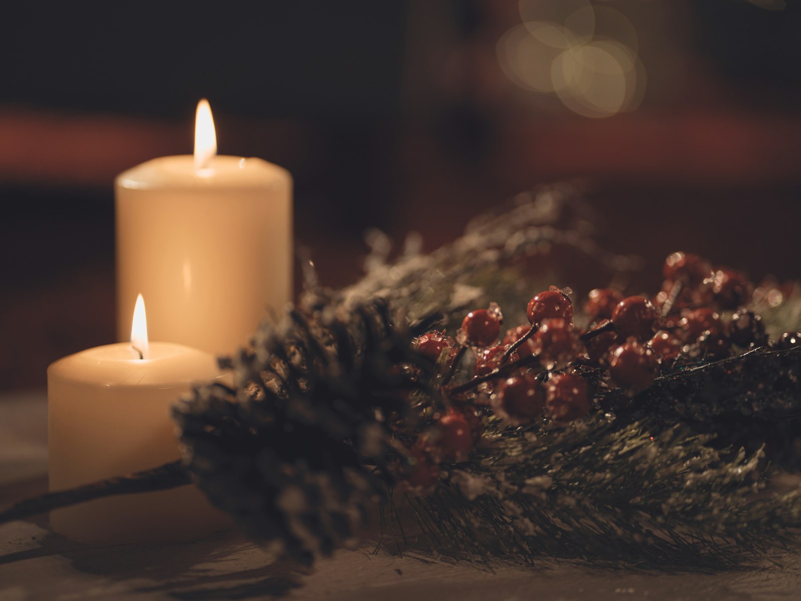 Pillar candles glowing beside a pine and red berry sprig for warm mantel lighting