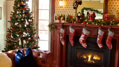 Christmas mantel decor with a garland, plaid stockings and a decorated tree beside a red fireplace