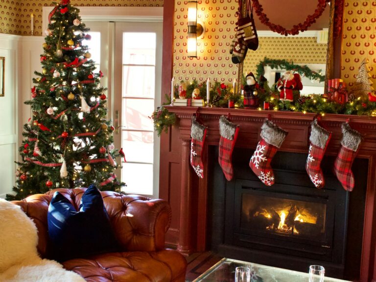 Christmas mantel decor with a garland, plaid stockings and a decorated tree beside a red fireplace