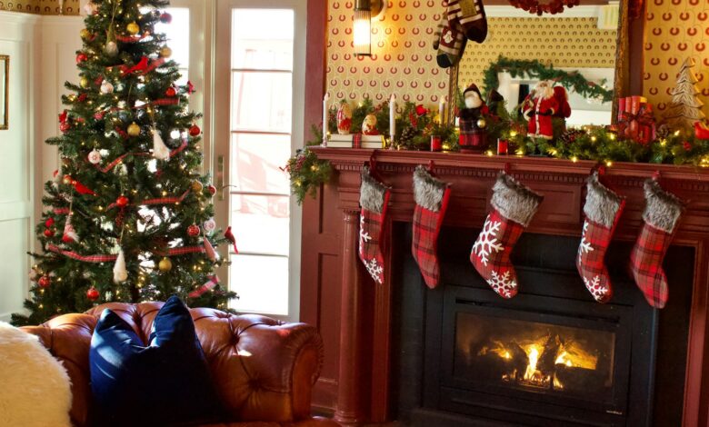 Christmas mantel decor with a garland, plaid stockings and a decorated tree beside a red fireplace