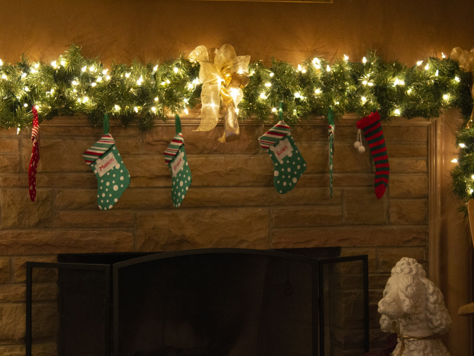Christmas mantel with a pre-lit garland, a gold bow and a row of knit stockings on a stone fireplace