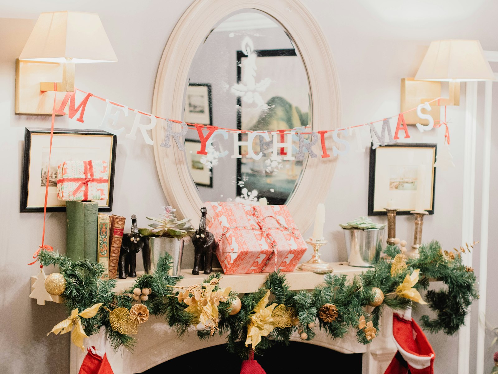 Oval mirror anchoring a Christmas mantel with a garland, a banner and wrapped gifts