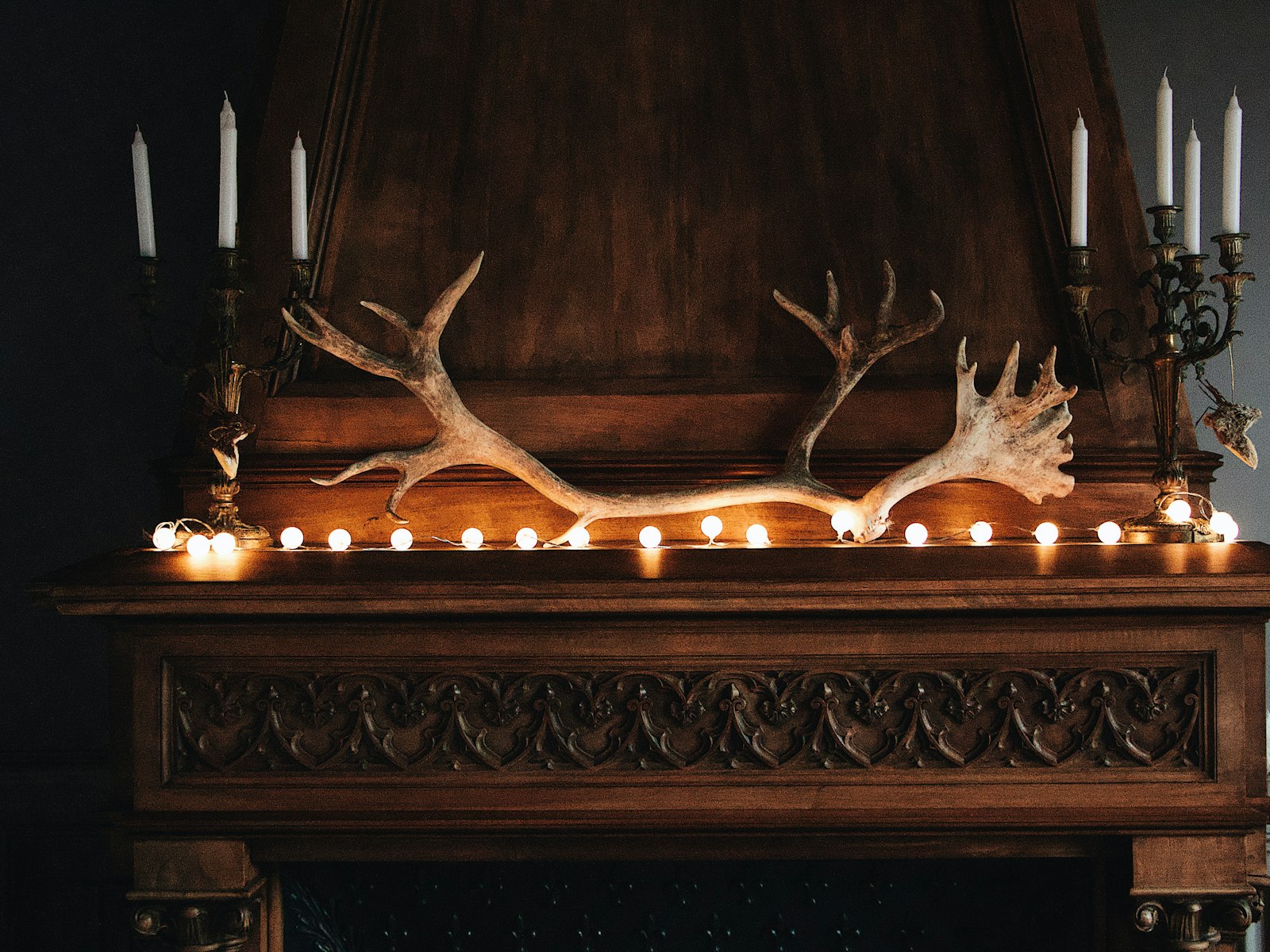 Wood mantel with tall taper candlesticks at each end, antlers and a row of string lights