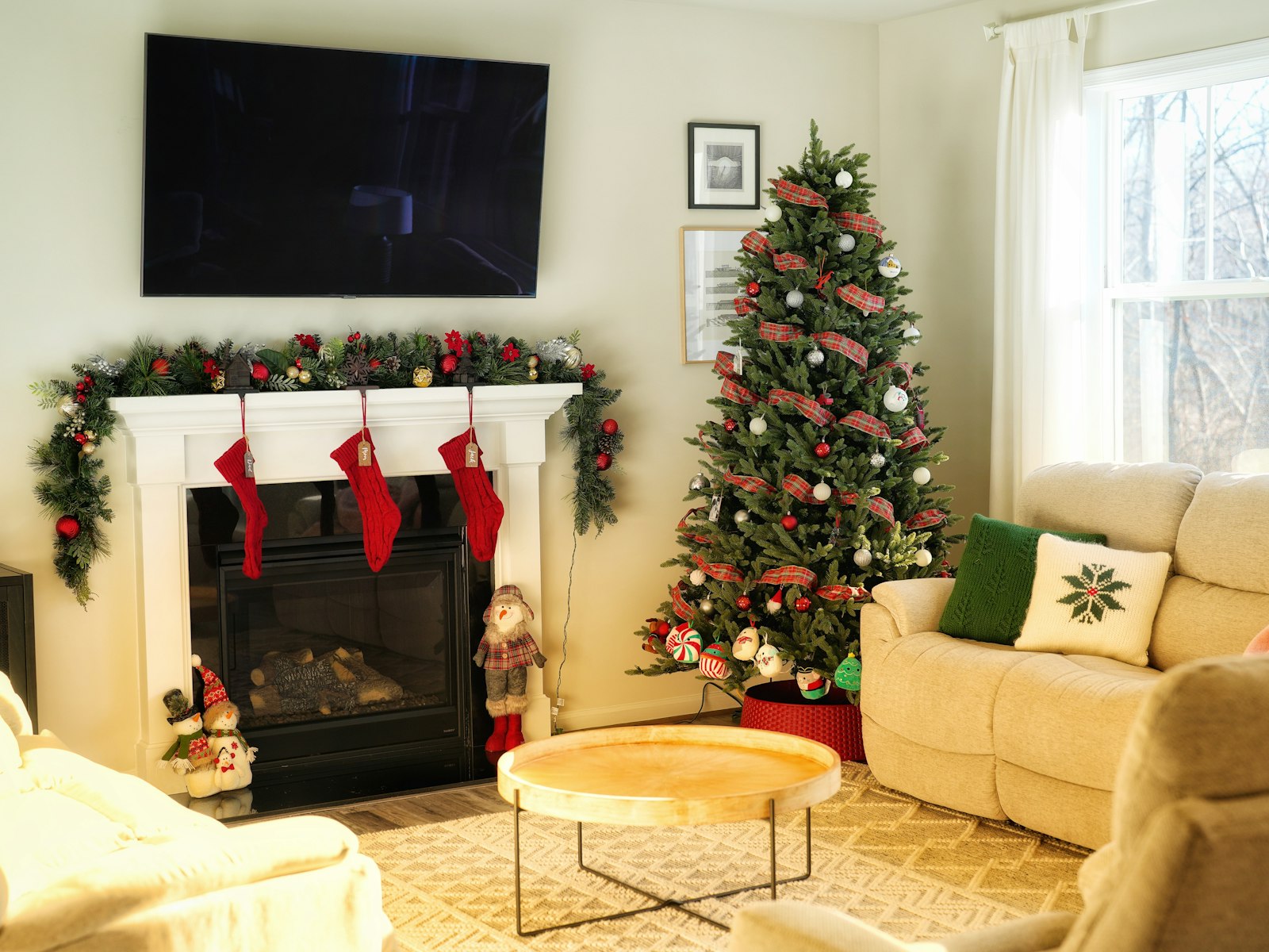 Christmas mantel with a TV above the fireplace, garland and red stockings below the screen