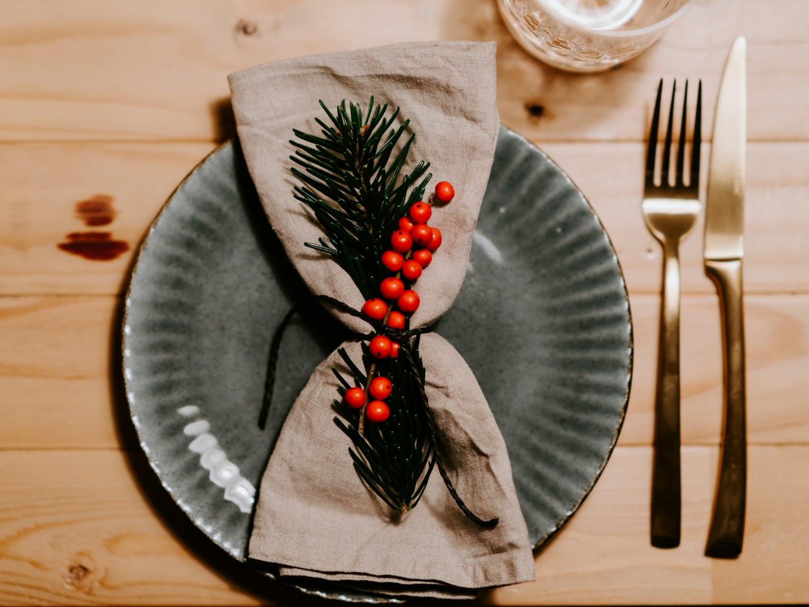 Linen napkin tied with a pine sprig and red berries on a grey plate
