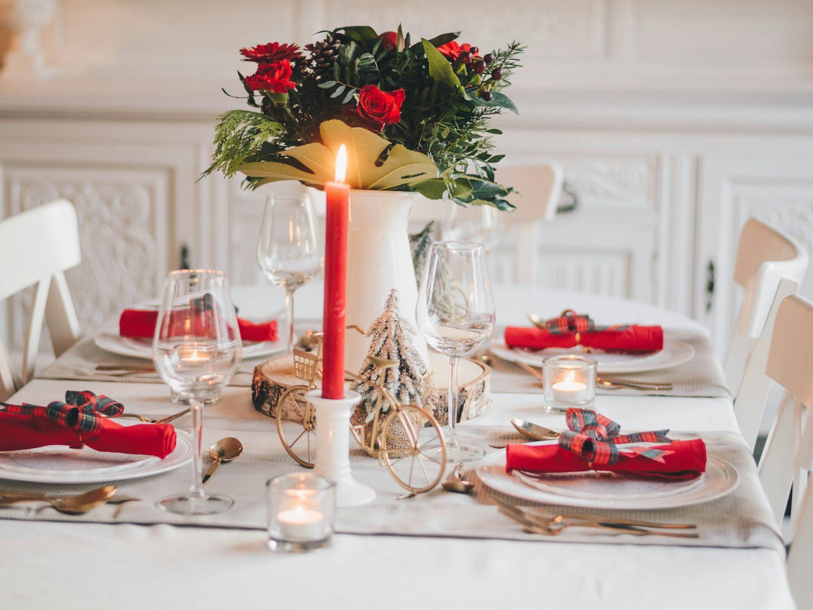 Christmas tablescape with red napkins, a red taper candle and a winter floral centerpiece on a white table