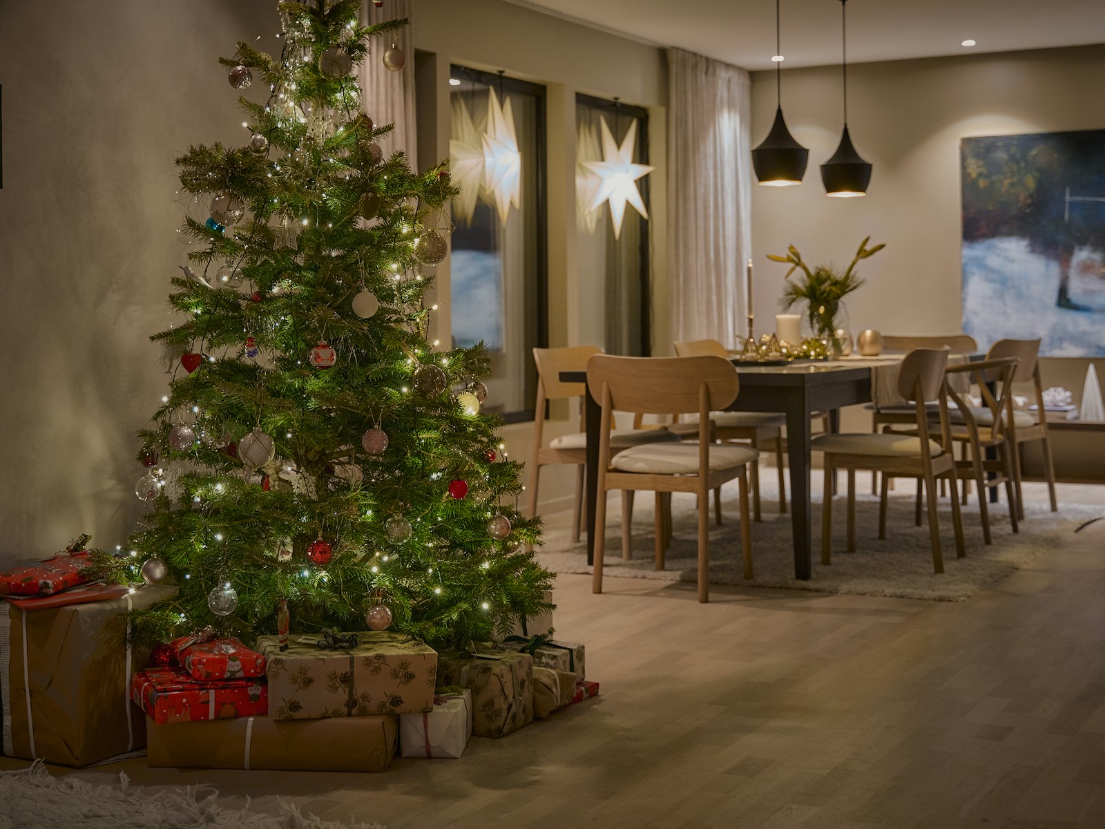 Decorated Christmas tree with warm lights and wrapped gifts in an open living and dining room