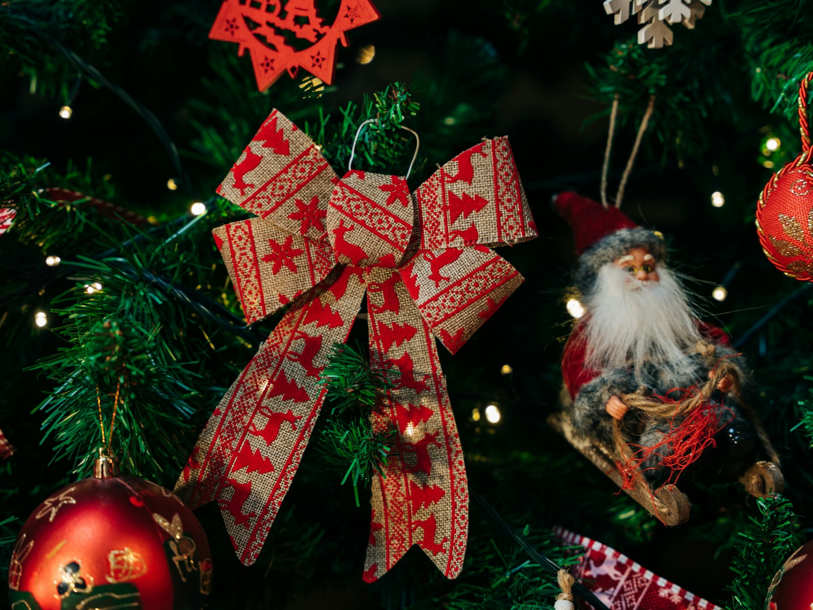 Christmas tree decorated with a red patterned ribbon bow, red ornaments and a vintage Santa