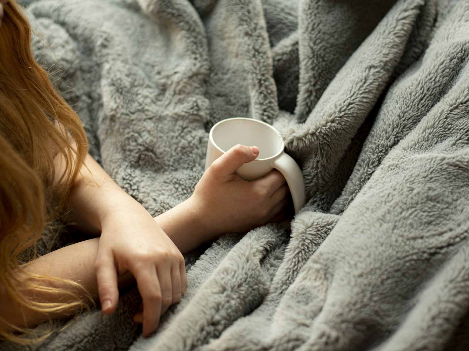 Hands holding a mug under a soft grey faux fur blanket