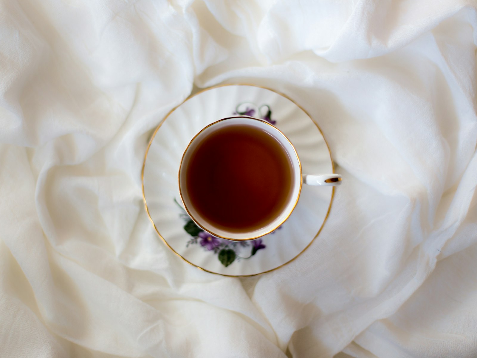 Cup of tea on a saucer resting on white bedding