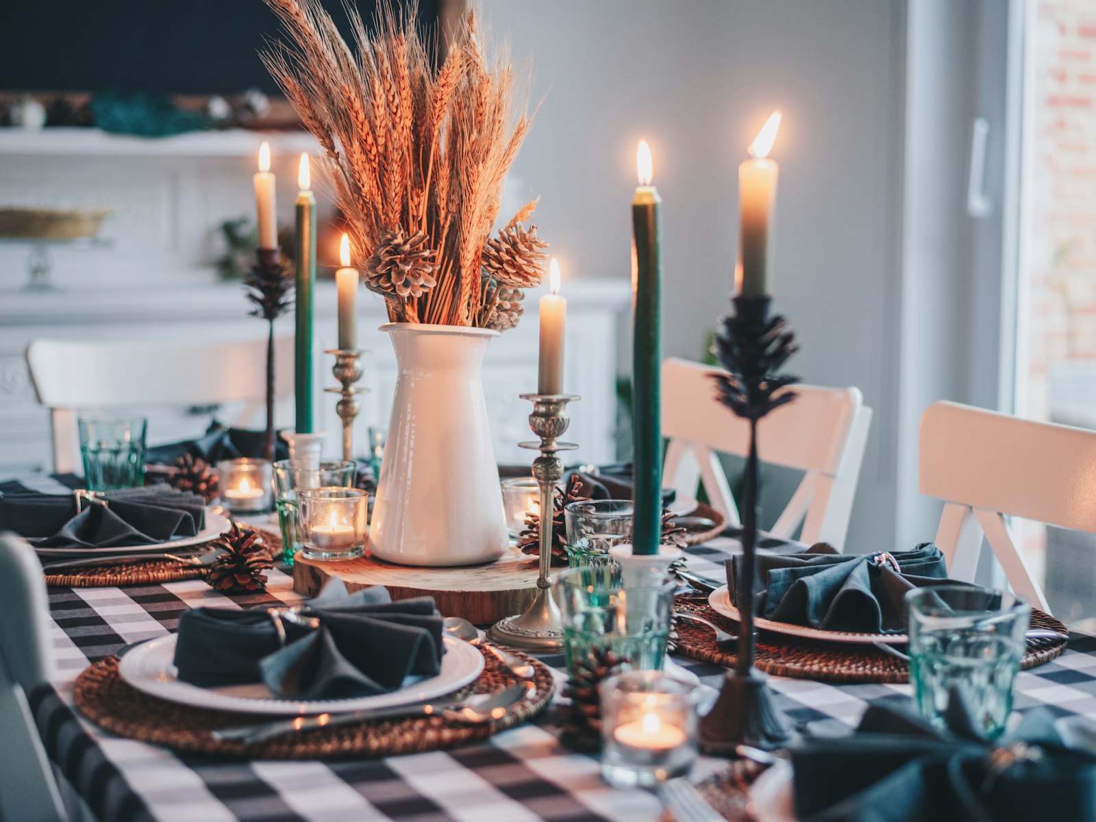 Fall dinner table with green and white taper candles and a pitcher of dried wheat