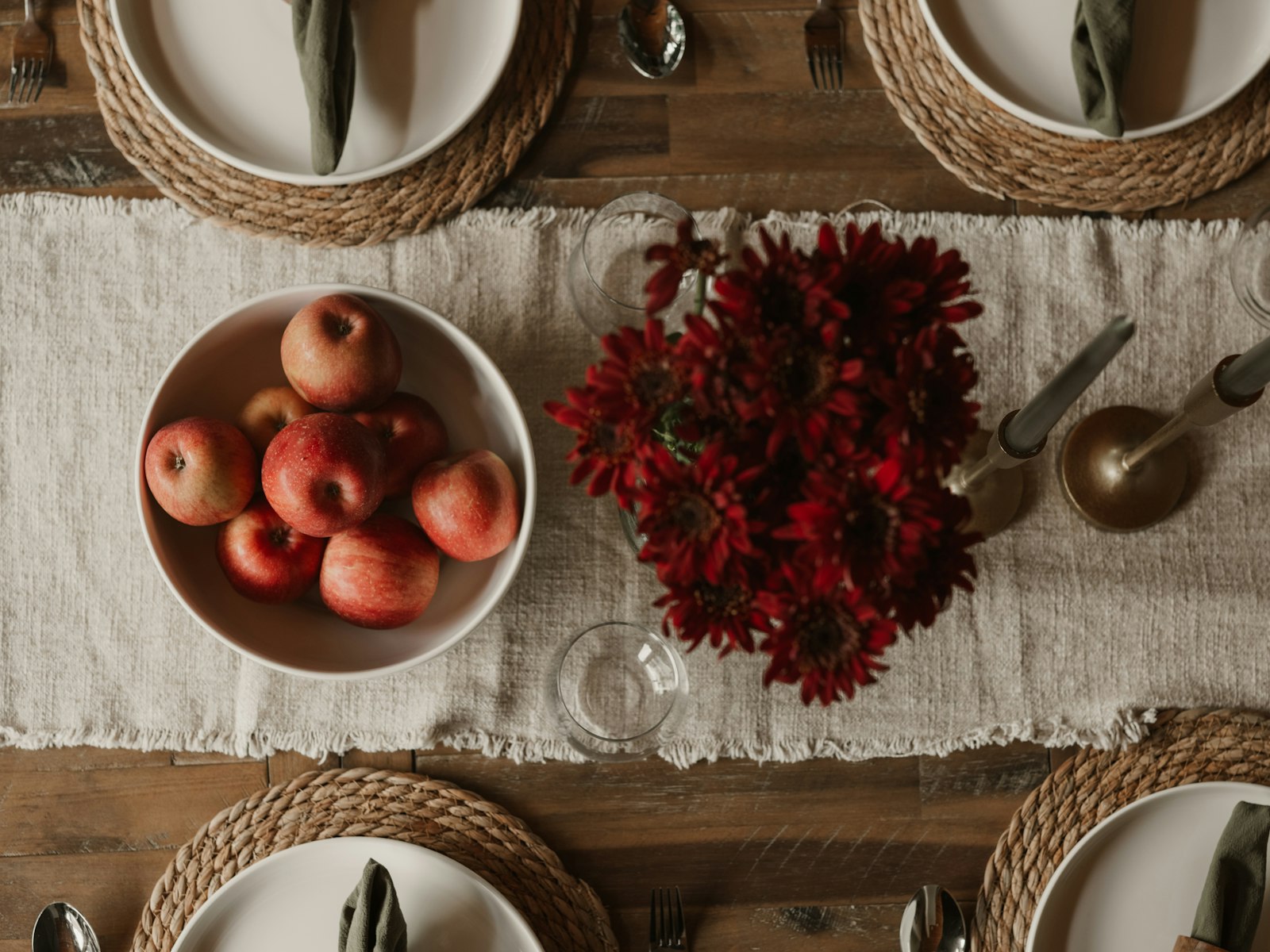 Linen table runner with a bowl of red apples, burgundy flowers and woven placemats