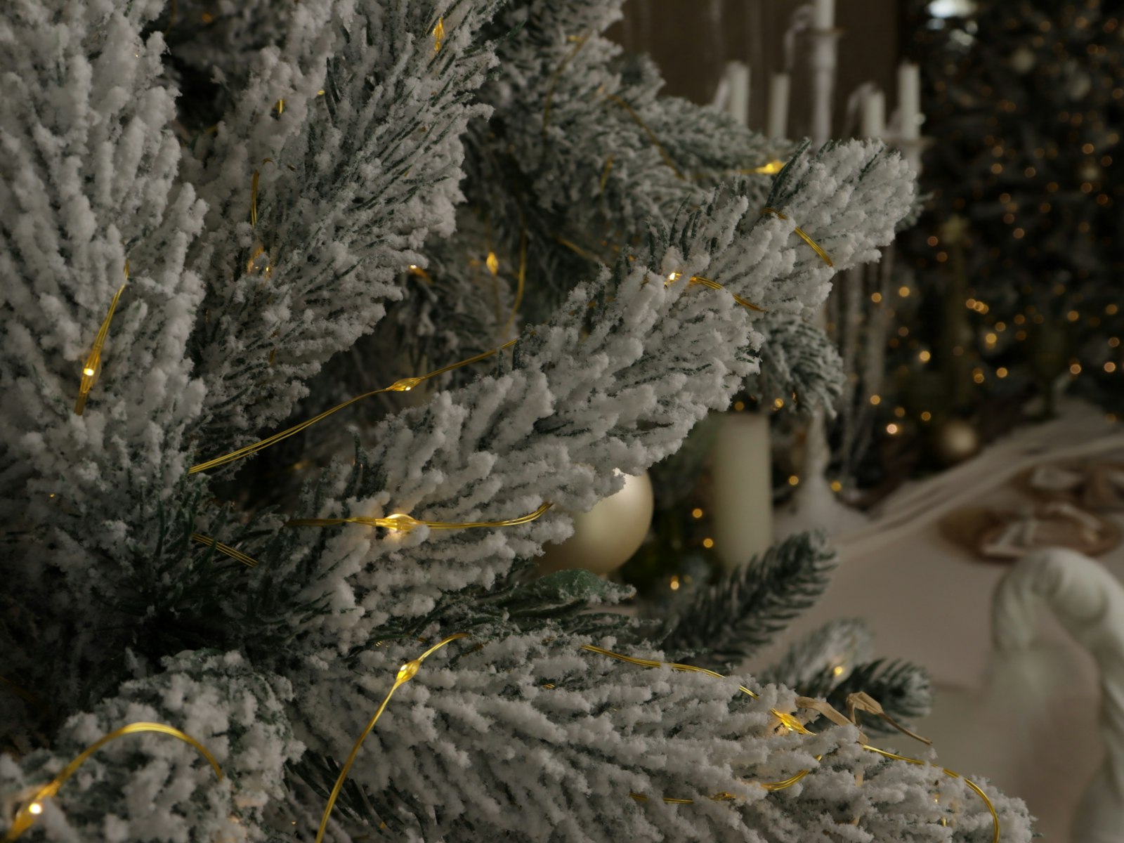 Flocked Christmas tree branches with warm fairy lights and cream ornaments