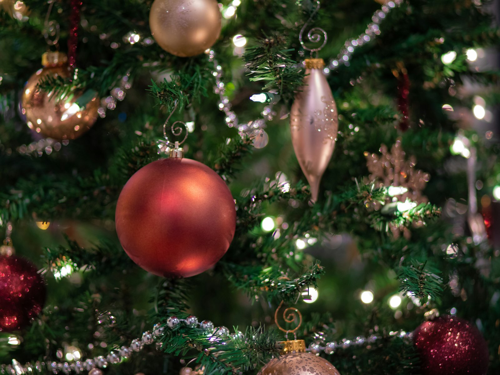 Glass Christmas ornaments in red and blush with a silver bead garland on a lit tree
