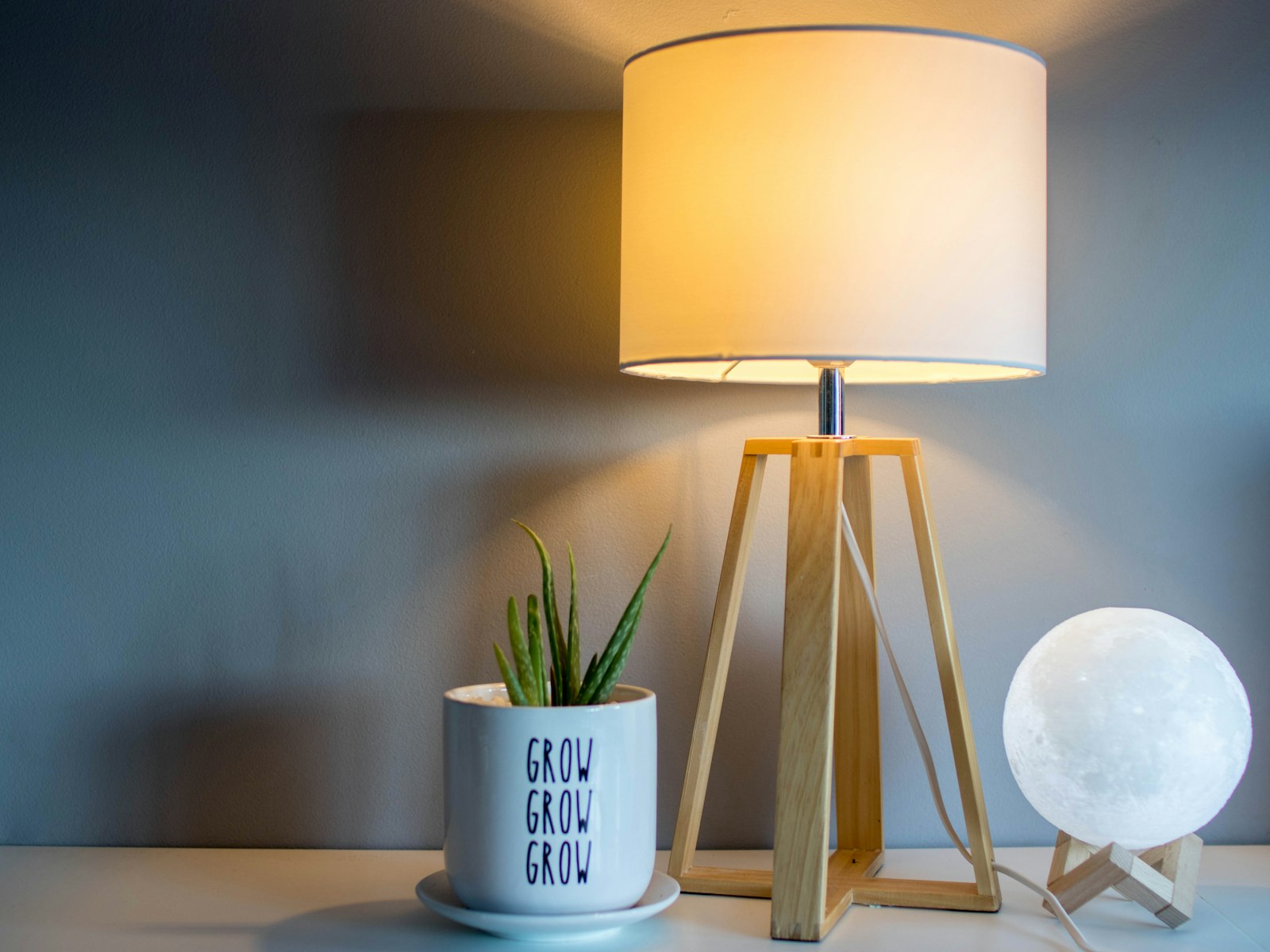Wood tripod table lamp glowing beside a small plant