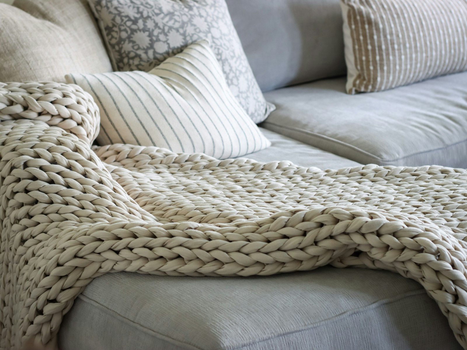 Cream knit throw layered over grey bedding and pillows
