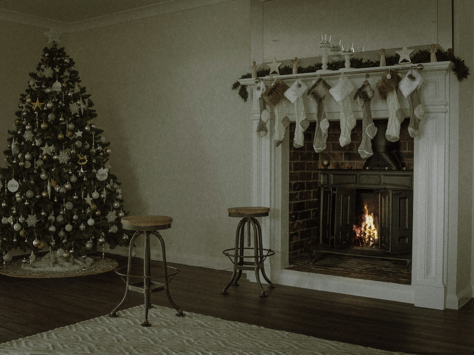Minimal white Christmas mantel with simple cream stockings, a lit fire and a white-ornament tree
