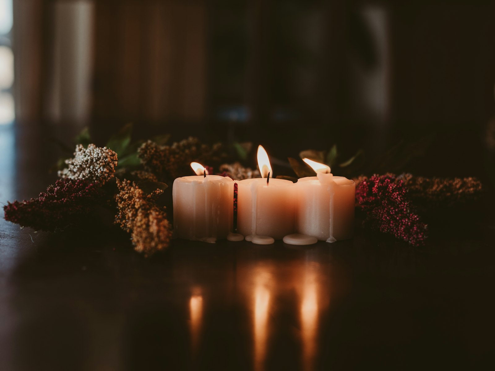 Moody Thanksgiving table lit by a cluster of pillar candles and dried flowers on dark wood