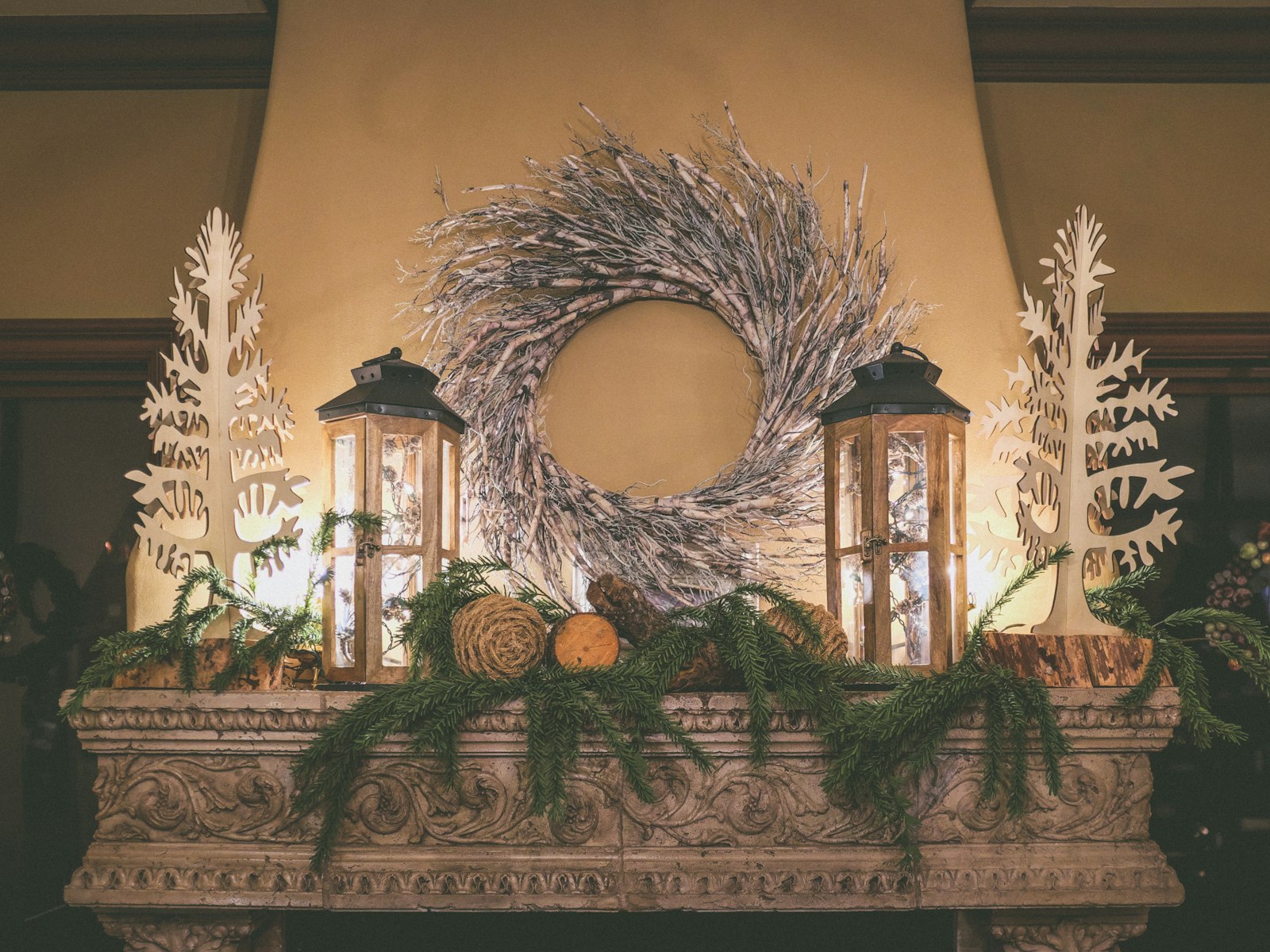 Natural Christmas mantel with fresh pine, pinecones, lanterns and a frosted twig wreath