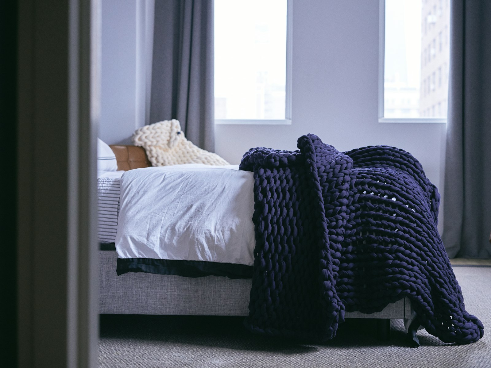 Navy chunky knit blanket draped over a white bed