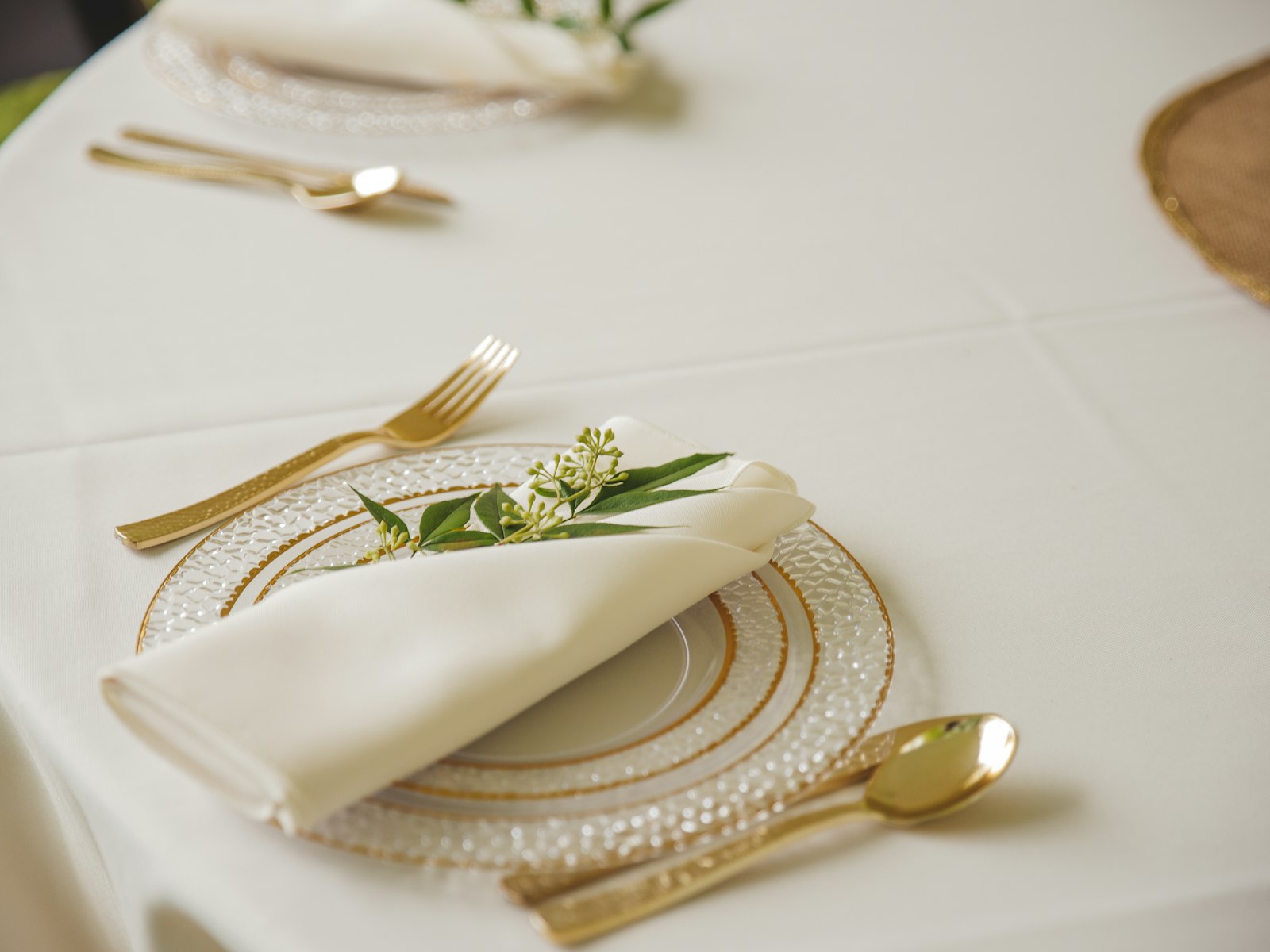 Neutral white Christmas place setting with gold flatware and a sprig of greenery on the napkin