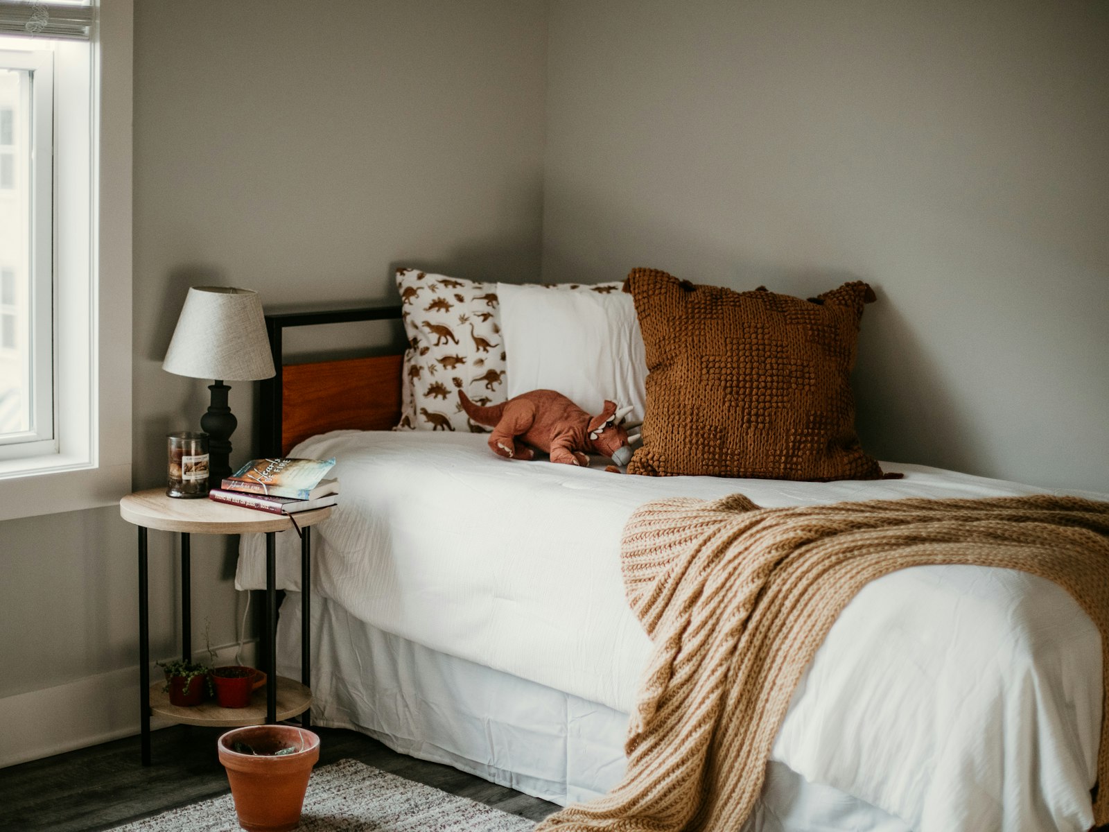 Neutral bedroom with a knit throw, rust pillows and a bedside lamp