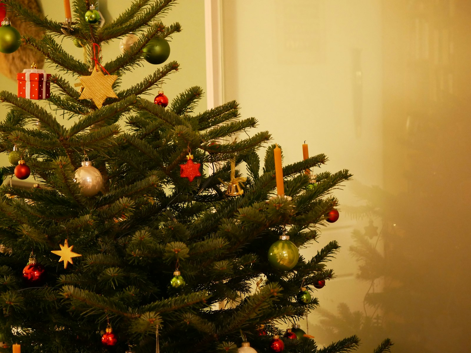 Real Christmas tree with straw stars, red baubles and gold ornaments by a warm wall
