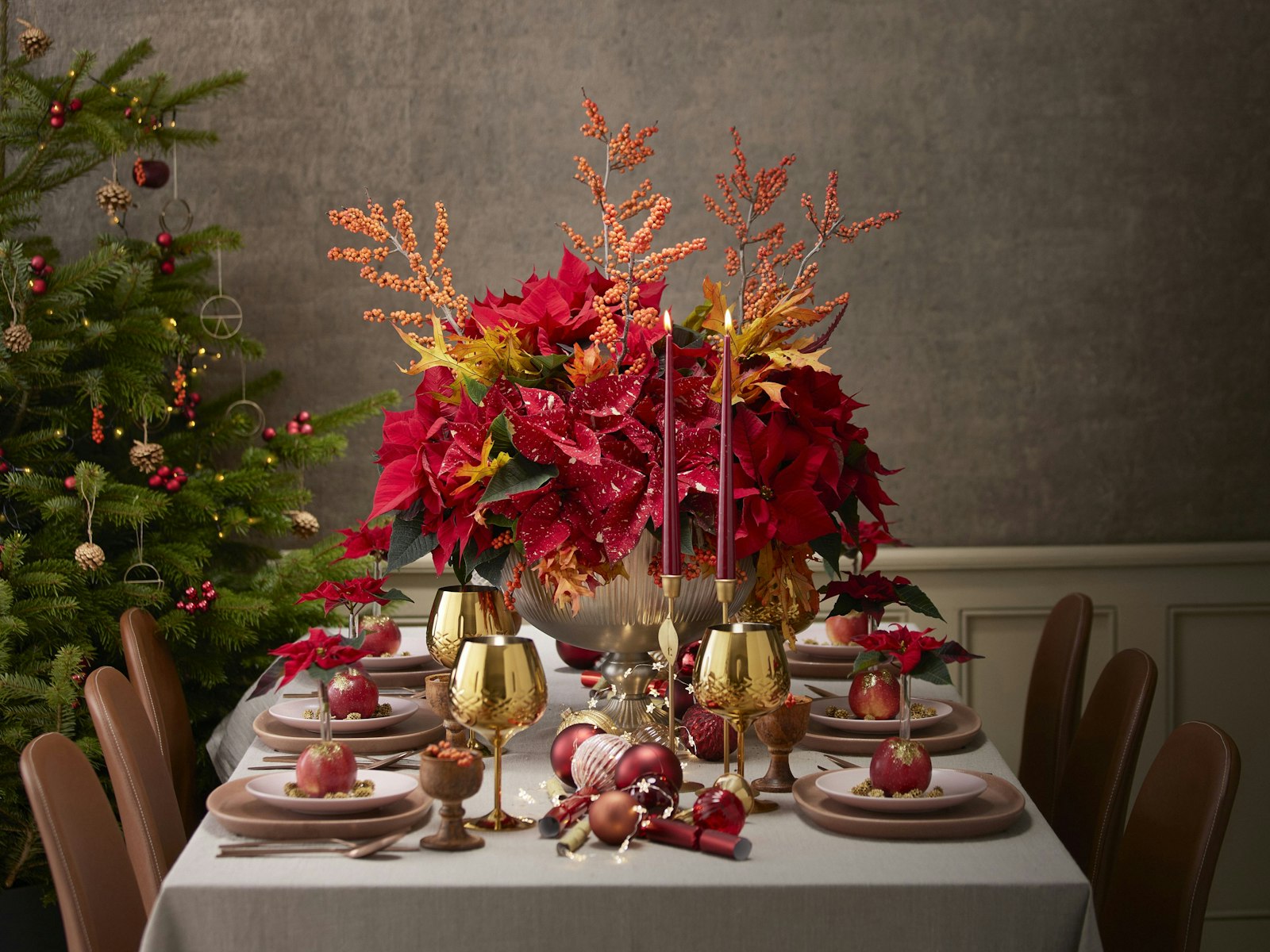 Classic red and gold Christmas table with a tall red floral centerpiece beside a decorated tree