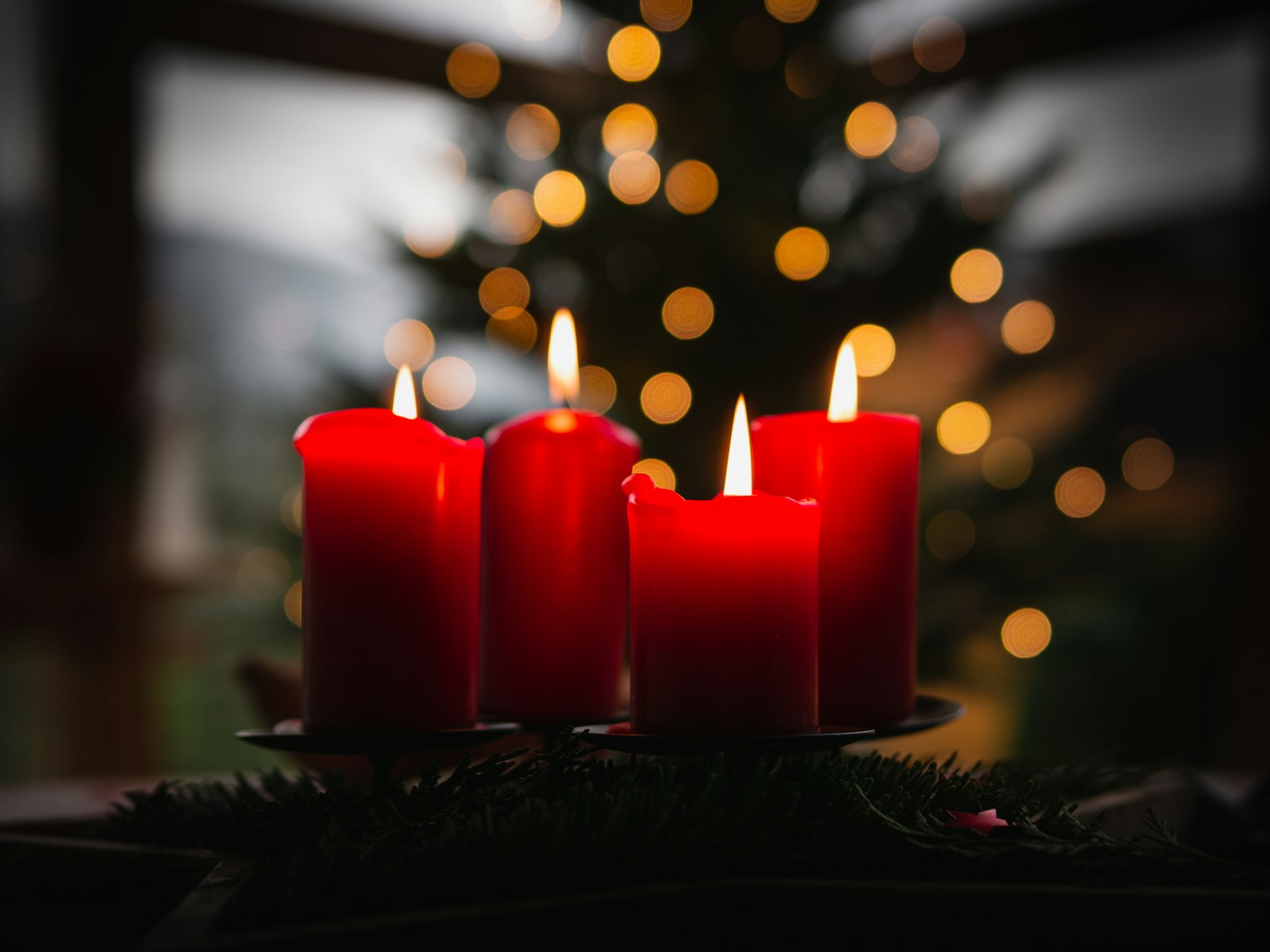 Red candles glowing in front of blurred Christmas tree lights