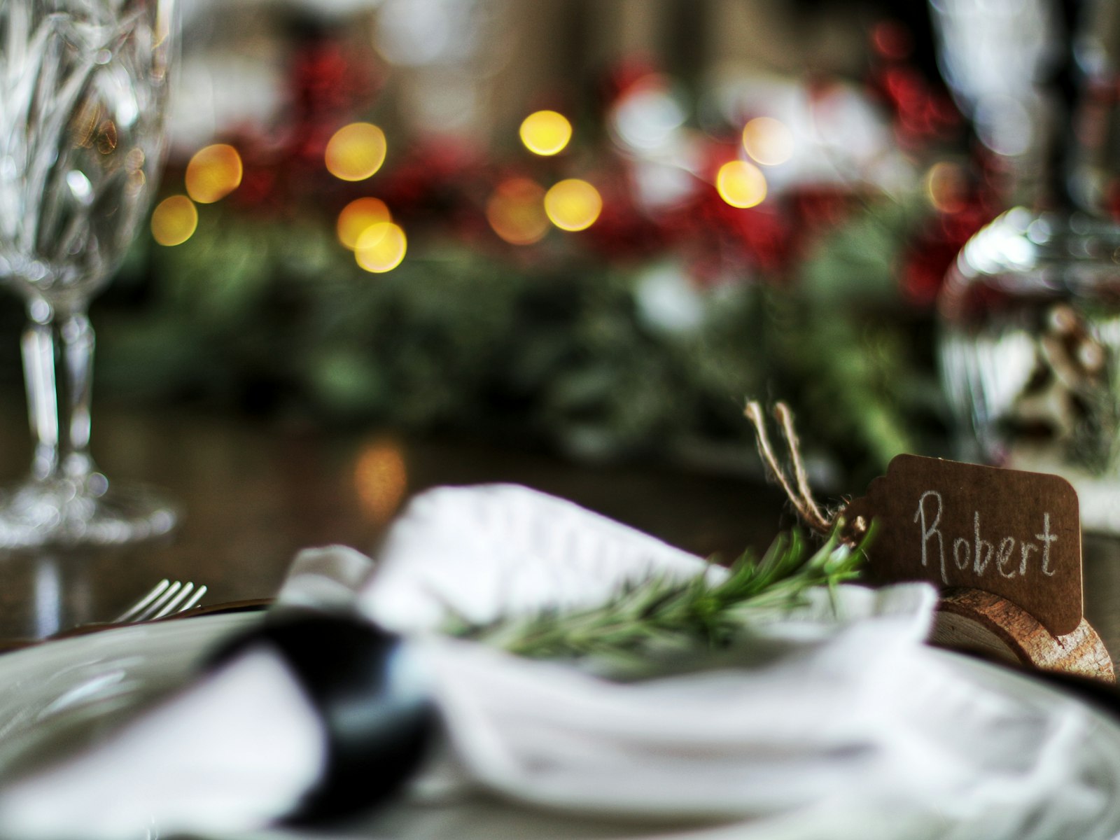 White napkin tied with rosemary and a handwritten name tag at a Christmas place setting