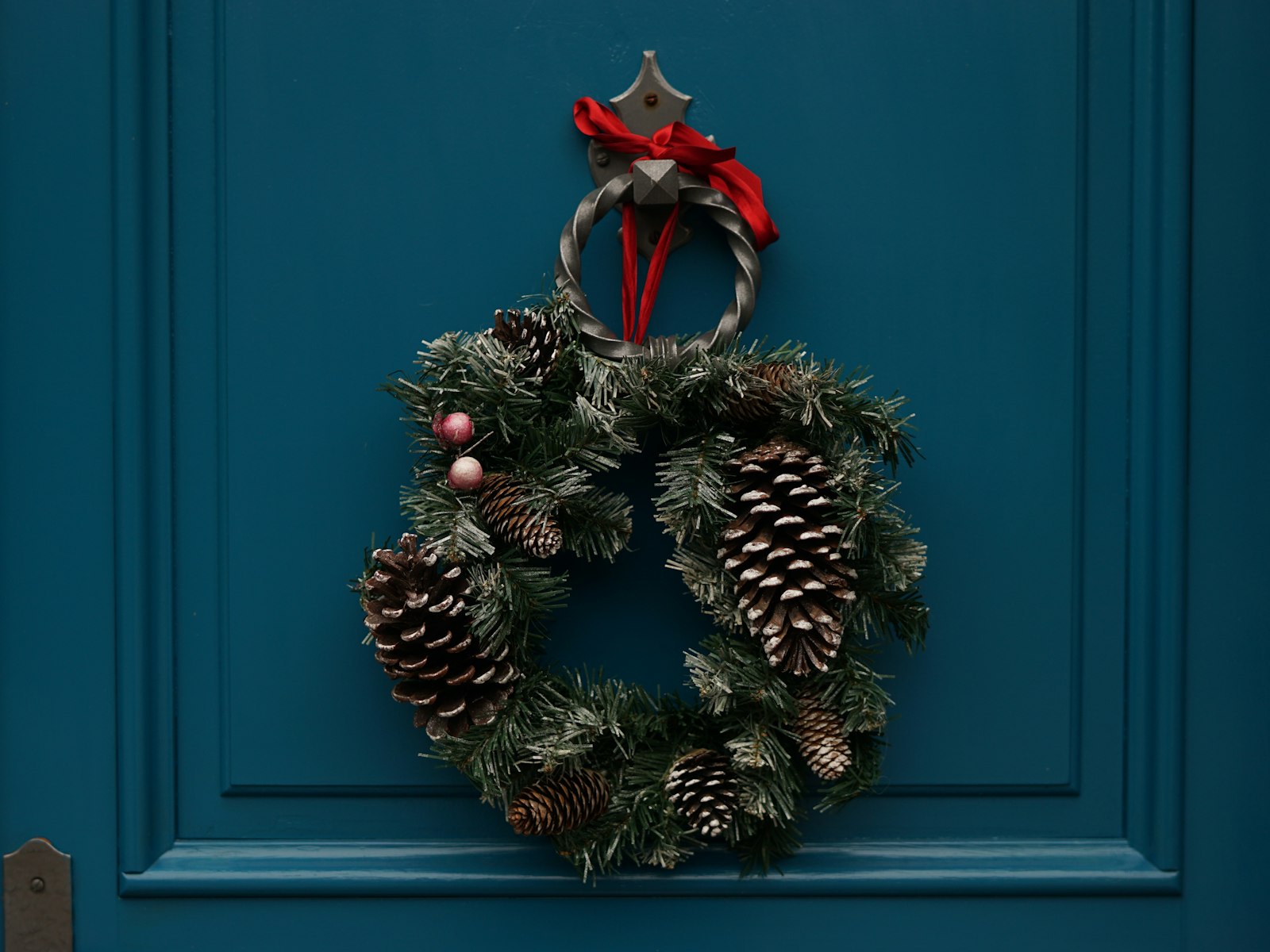 Teal front door with a pinecone and ribbon Christmas wreath