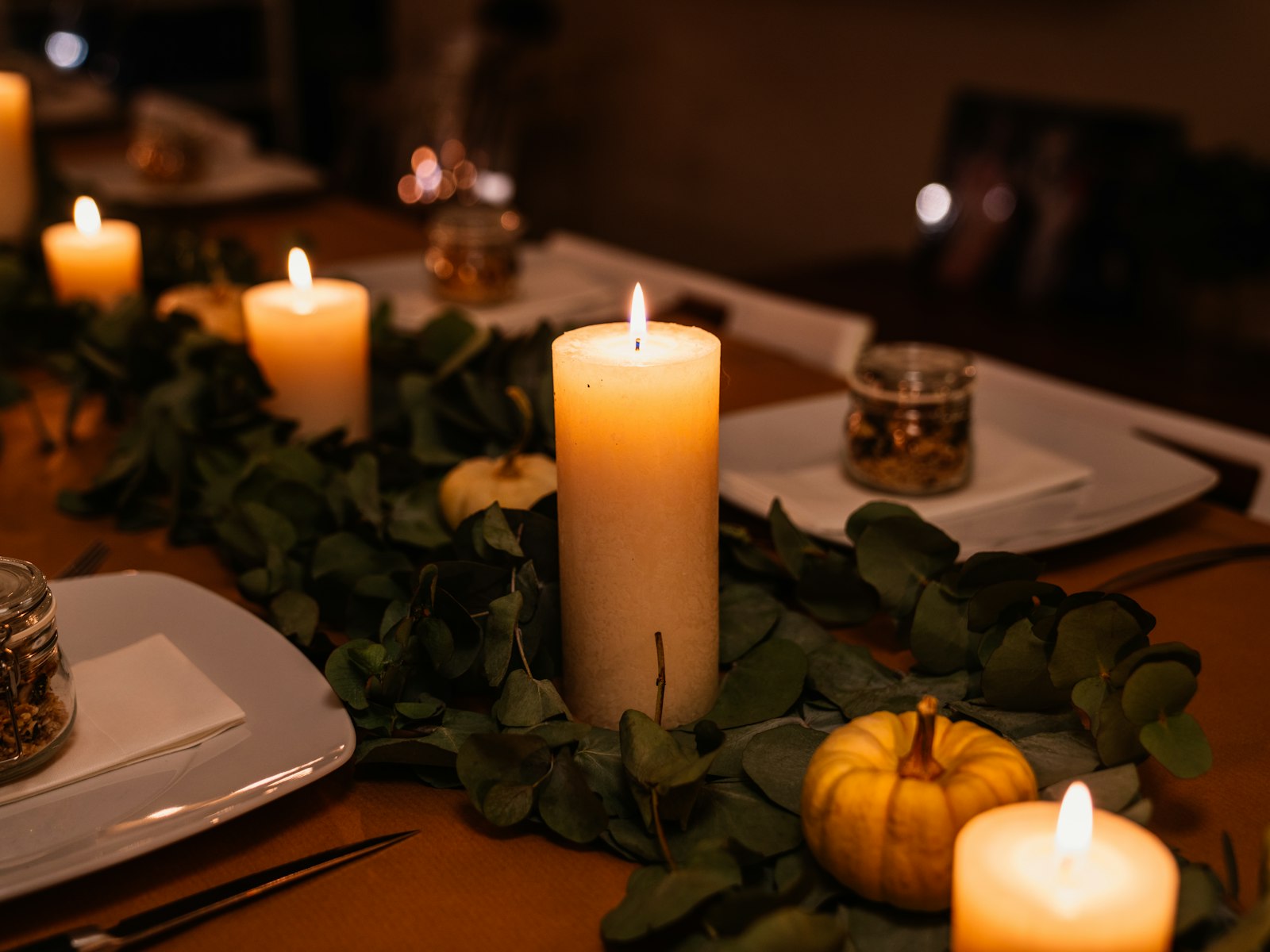 Thanksgiving table with a greenery garland runner, pillar candles and mini pumpkins