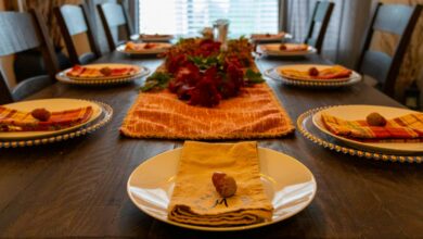 Thanksgiving table decor with an orange runner, red flower centerpiece and folded napkins on gold chargers
