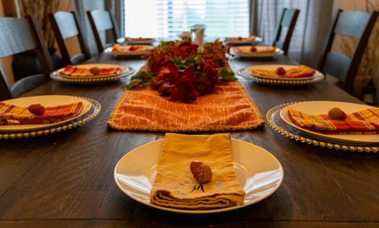 Thanksgiving table decor with an orange runner, red flower centerpiece and folded napkins on gold chargers
