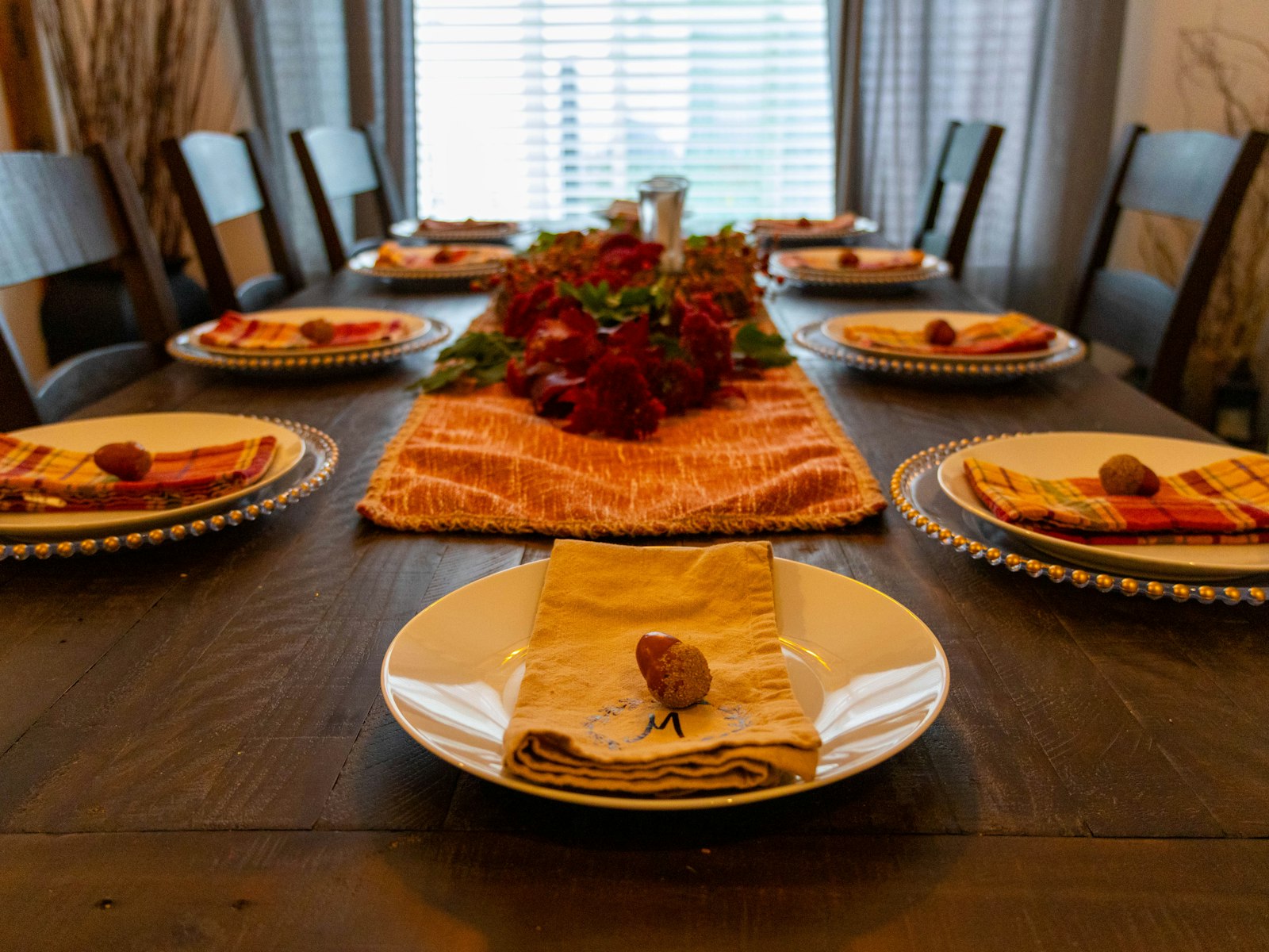 Thanksgiving table decor with an orange runner, red flower centerpiece and folded napkins on gold chargers