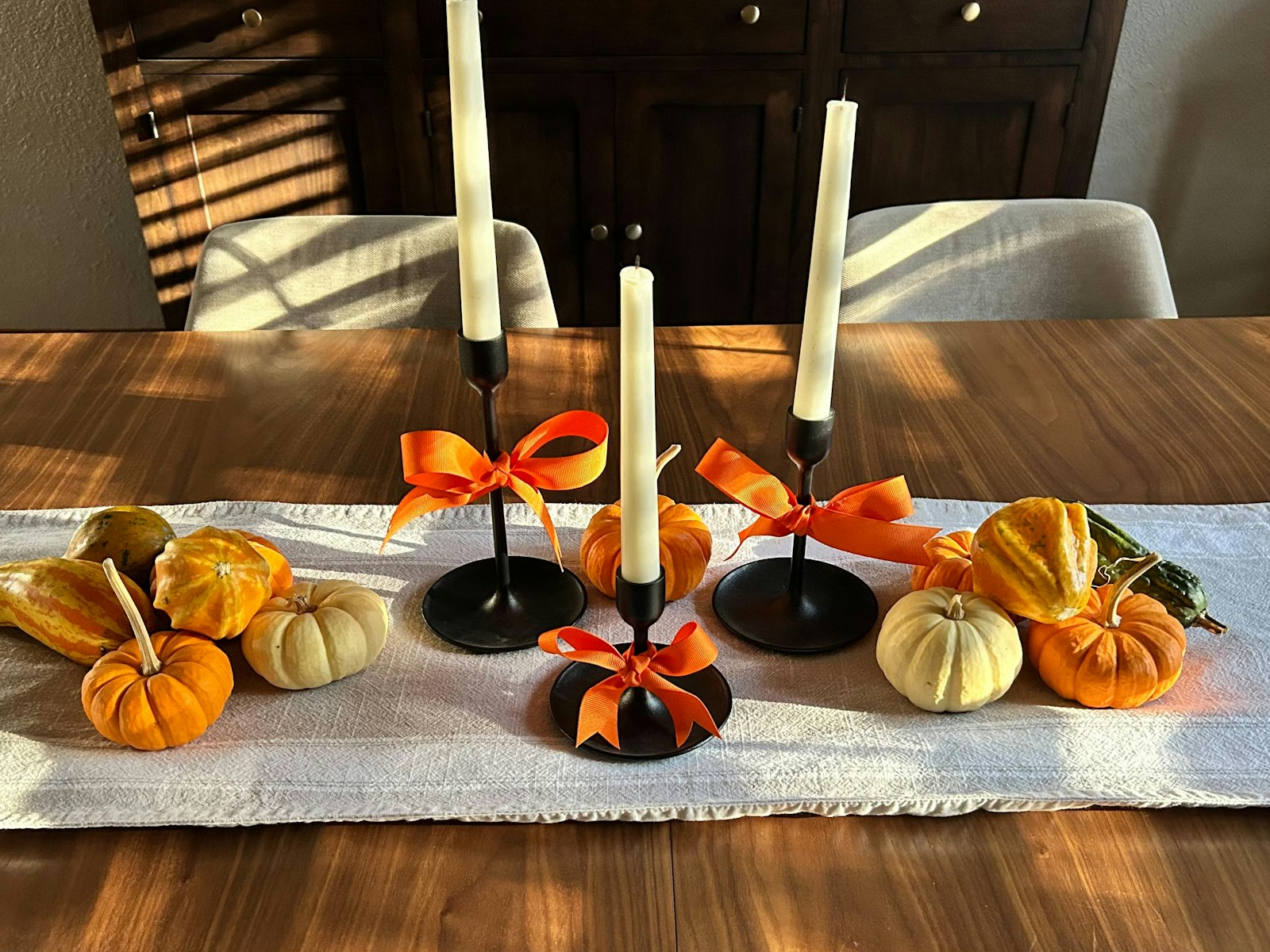 Candle centerpiece of black taper candlesticks with orange bows and mini pumpkins on a linen runner