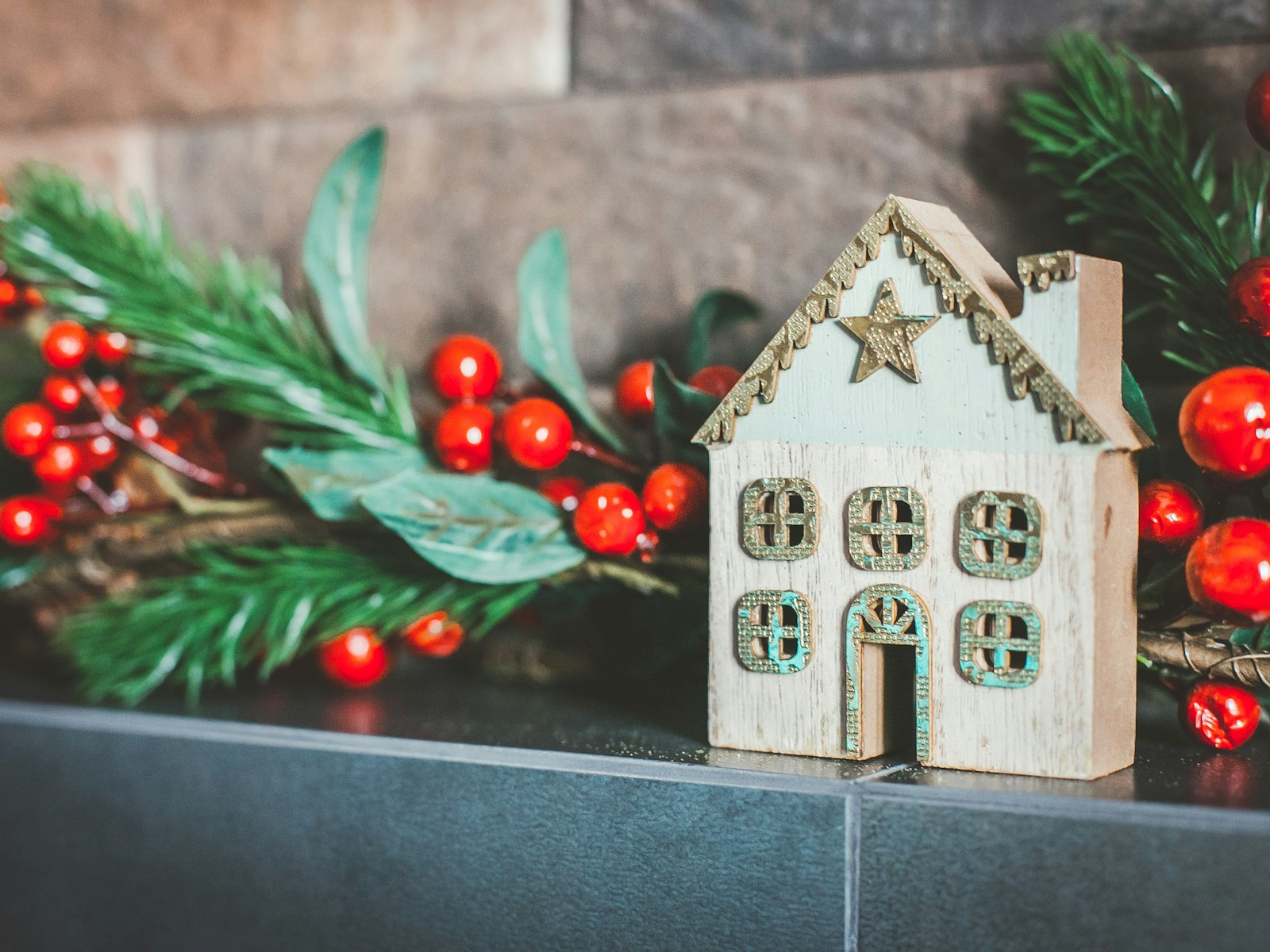 Vintage-style Christmas mantel with a little wooden house, red berries and greenery